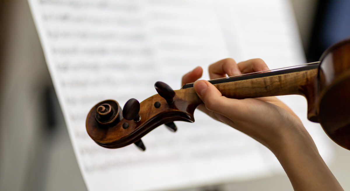 Woman violinist playing an antique baroque violin in a close up over the shoulder view of her hand on the strings against a backdrop of a music score during a recital